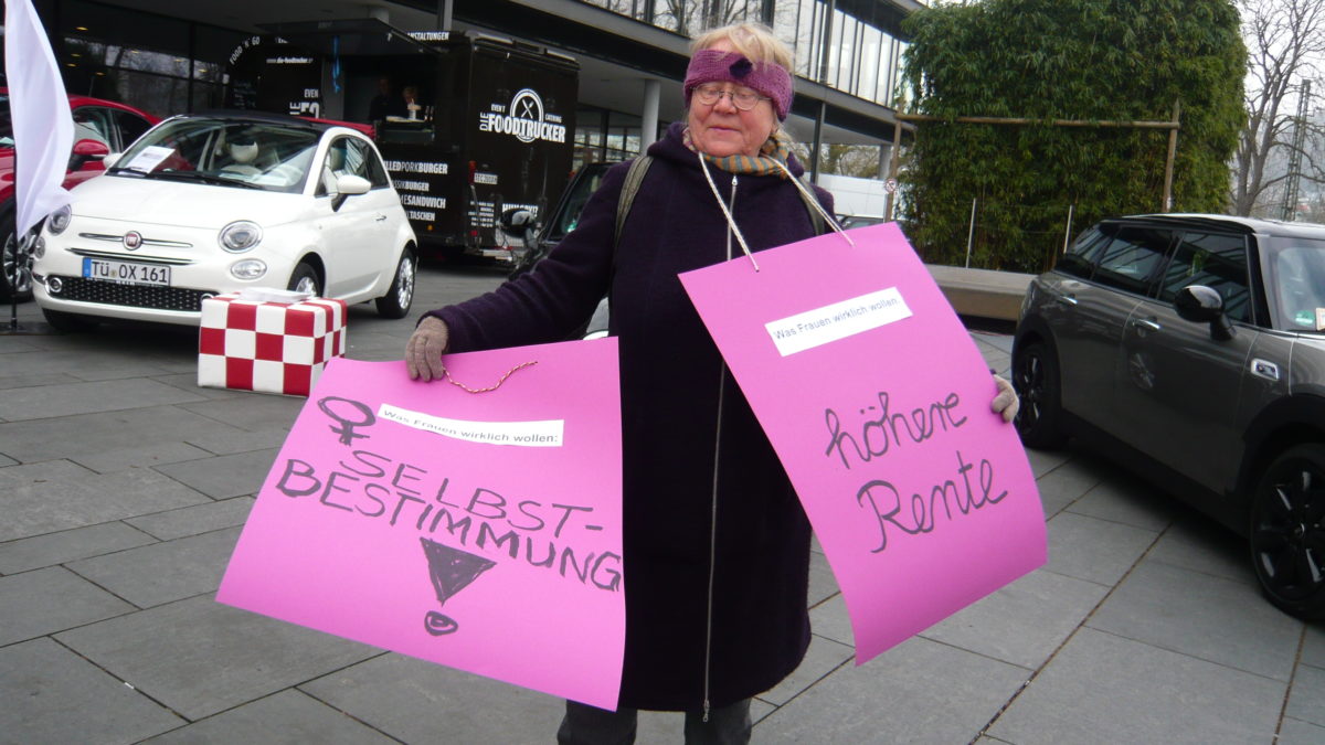 Frau mit zwei pinkfarbenen Transparenten. Auf ihnen steht, was Frauen wirklich wollen: höhere Rente und Selbstbestimmung